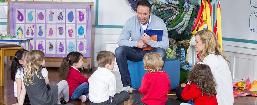 一个拿着书的人坐在地板上和孩子们说话.